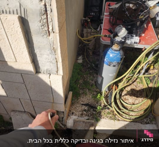 אדם מחזיק מכשיר מדידה ליד צינור ליד קיר